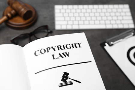 Book with words COPYRIGHT LAW, computer keyboard and gavel on table, closeup