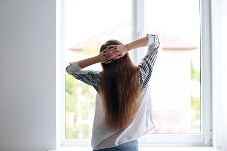 Young beautiful woman standing near window at homeの写真素材