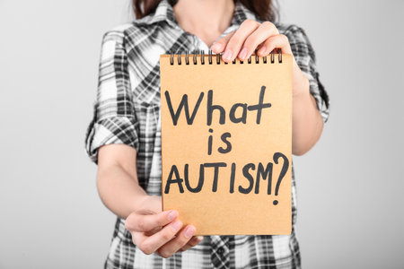 Woman holding notebook with words WHAT IS AUTISM on light backgroundの写真素材