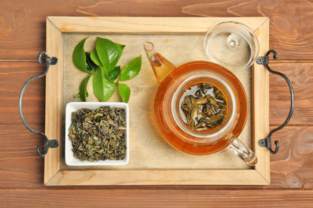 Wooden tray with hot aromatic tea, dry and fresh leaves on wooden table, top viewの写真素材