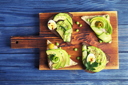 Tasty crispy toasts with avocado on wooden board, top view