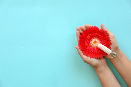 Woman holding flower and tampon on color background, top view. Gynecological careの写真素材