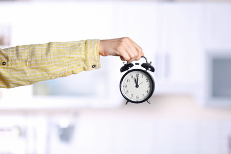 Young woman holding alarm clock on blurred background. time conceptの写真素材