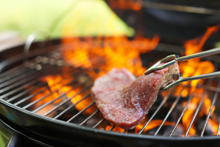 Tasty meat on barbecue grill with fire flames outdoors, closeupの写真素材