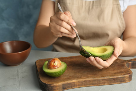Woman scooping ripe avocado with spoon at tableの写真素材