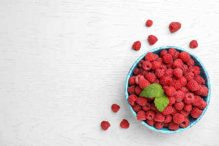 Bowl with ripe aromatic raspberries on wooden table, top view