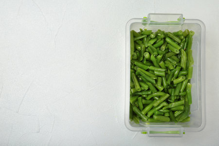Plastic container with frozen green beans on light background, top view. vegetable preservation
