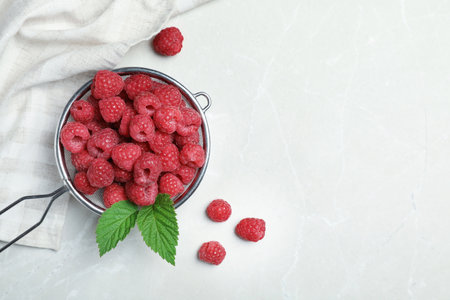 Sieve with ripe aromatic raspberries on table, top view