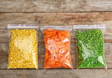 Plastic bags with frozen vegetables on wooden background, top viewの写真素材