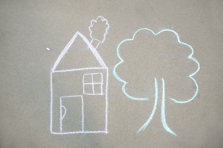 Child's chalk drawing of house and tree on asphalt, top viewの写真素材