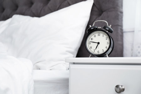 Analog alarm clock on table in bedroom. Time of day