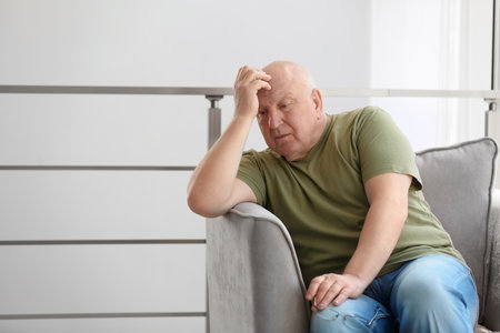 Depressed senior man sitting in armchair indoorsの写真素材