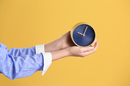 Young woman holding alarm clock on color background. time concept