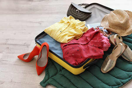 Open suitcase with clothes and accessories on floorの写真素材