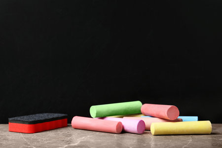Color pieces of chalk and duster on table near blackboardの写真素材