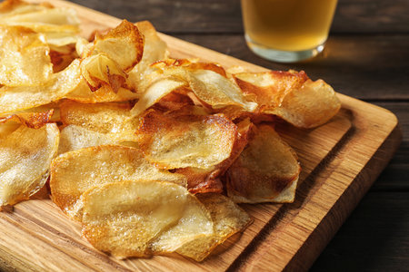 Wooden board with crispy potato chips on table, closeupの写真素材