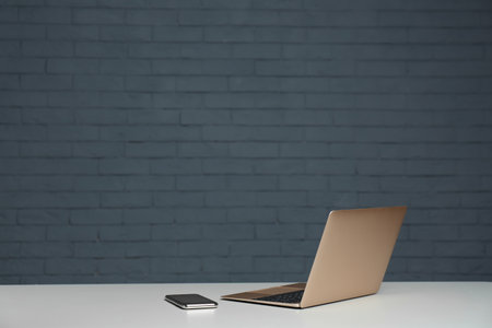 Modern laptop and mobile phone on table against brick wallの写真素材