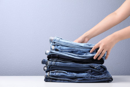 Young woman folding stylish jeans on tableの写真素材