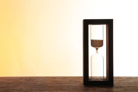 Hourglass with flowing sand on table against light background. time management