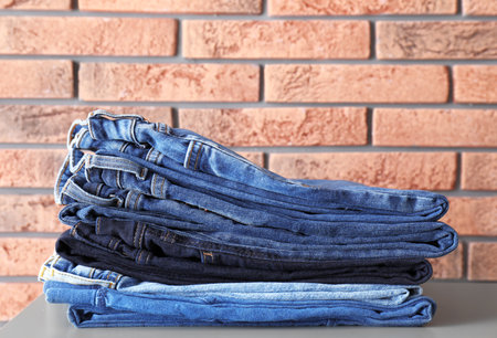 Stack of jeans on table against brick wall backgroundの写真素材