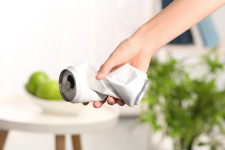 Woman holding crumpled aluminum can on blurred background. metal waste recycling