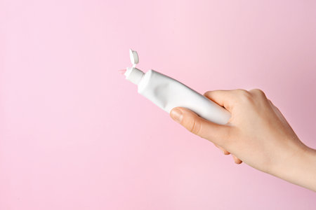 Woman holding tube of toothpaste on color background