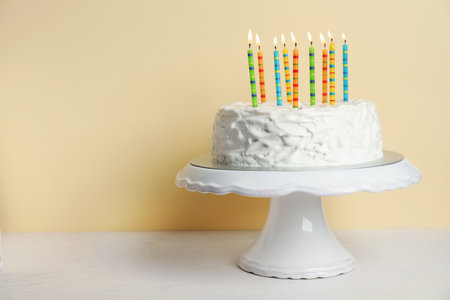 Birthday cake with candles on table against color backgroundの写真素材