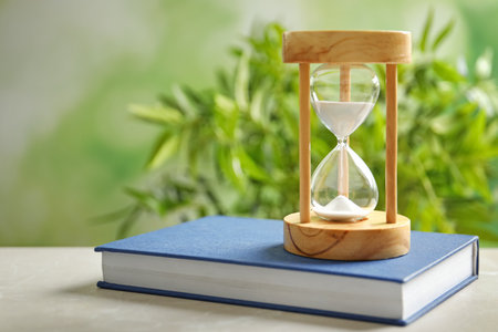 Hourglass and book on table against blurred background. time managementの写真素材
