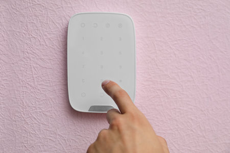 Young man entering code on alarm system keypad indoors