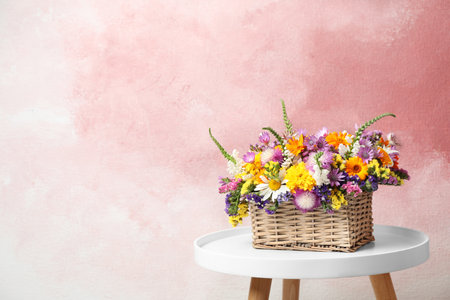 Wicker basket with beautiful wild flowers on table against color backgroundの写真素材