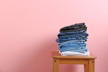 Stack of different jeans on stool against color backgroundの写真素材