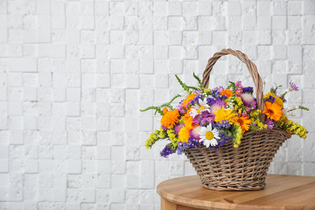 Wicker basket with beautiful wild flowers on table near white wallの写真素材