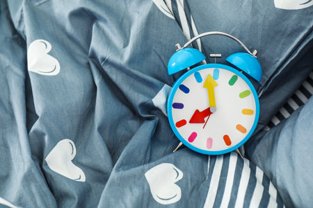 Analog alarm clock on bed, top view. Time of dayの写真素材