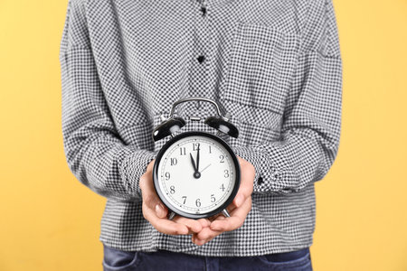 Young woman holding clock on color background. time management