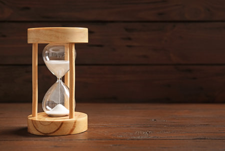 Hourglass with flowing sand on table against black background. time management