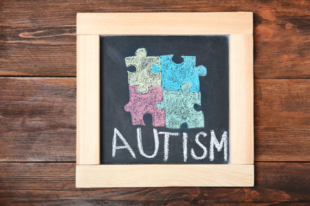 Chalkboard with word AUTISM and drawn puzzle pieces on wooden backgroundの写真素材