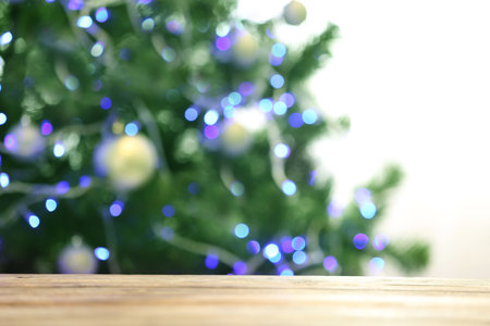 Blurred view of fir tree with glowing Christmas lights near table indoors. Festive mood