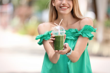Young woman with plastic cup of healthy smoothie outdoorsの写真素材