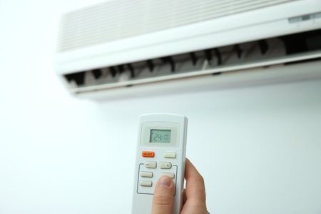 Man operating air conditioner with remote control indoorsの写真素材