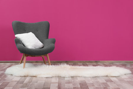 Comfortable armchair with white cushion and rug against color wallの写真素材