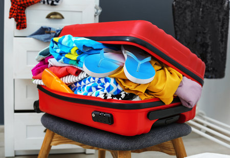 Suitcase with beach clothes and accessories on stool indoorsの写真素材