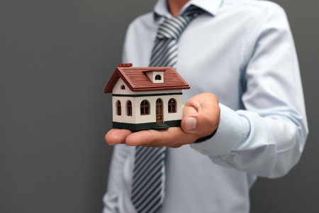 Real estate agent holding house model on gray backgroundの写真素材