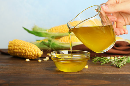 Woman pouring fresh corn oil into bowl on wooden tableの写真素材