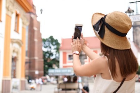 Young woman taking photo of building on city streetの写真素材