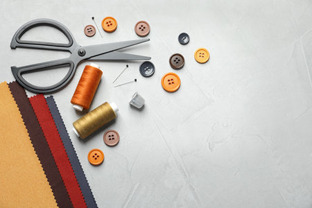 Set of tailoring accessories and fabric on light background, top view