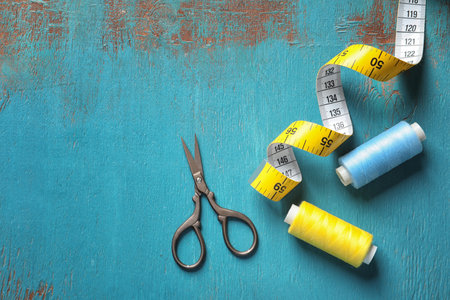 Measuring tape, scissors and threads on wooden background, top view. tailoring equipment