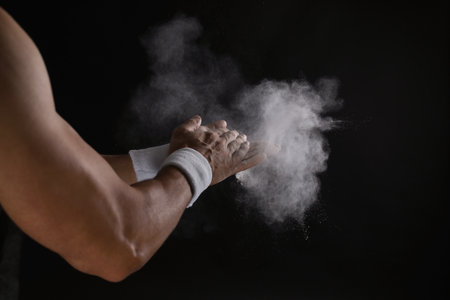 Young man applying chalk powder on hands against dark backgroundの写真素材
