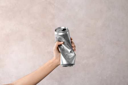 Woman holding crumpled aluminum can on light background. metal waste recycling
