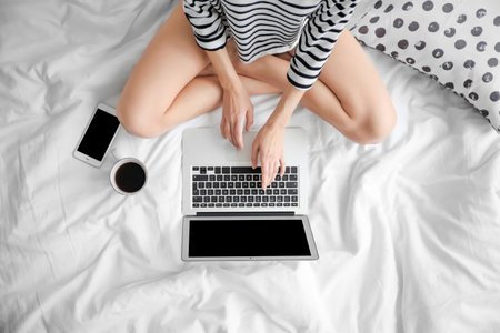 Female blogger with laptop and cup of coffee on bed, top viewの写真素材