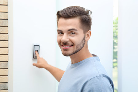 Young man pressing fingerprint scanner on alarm system indoors